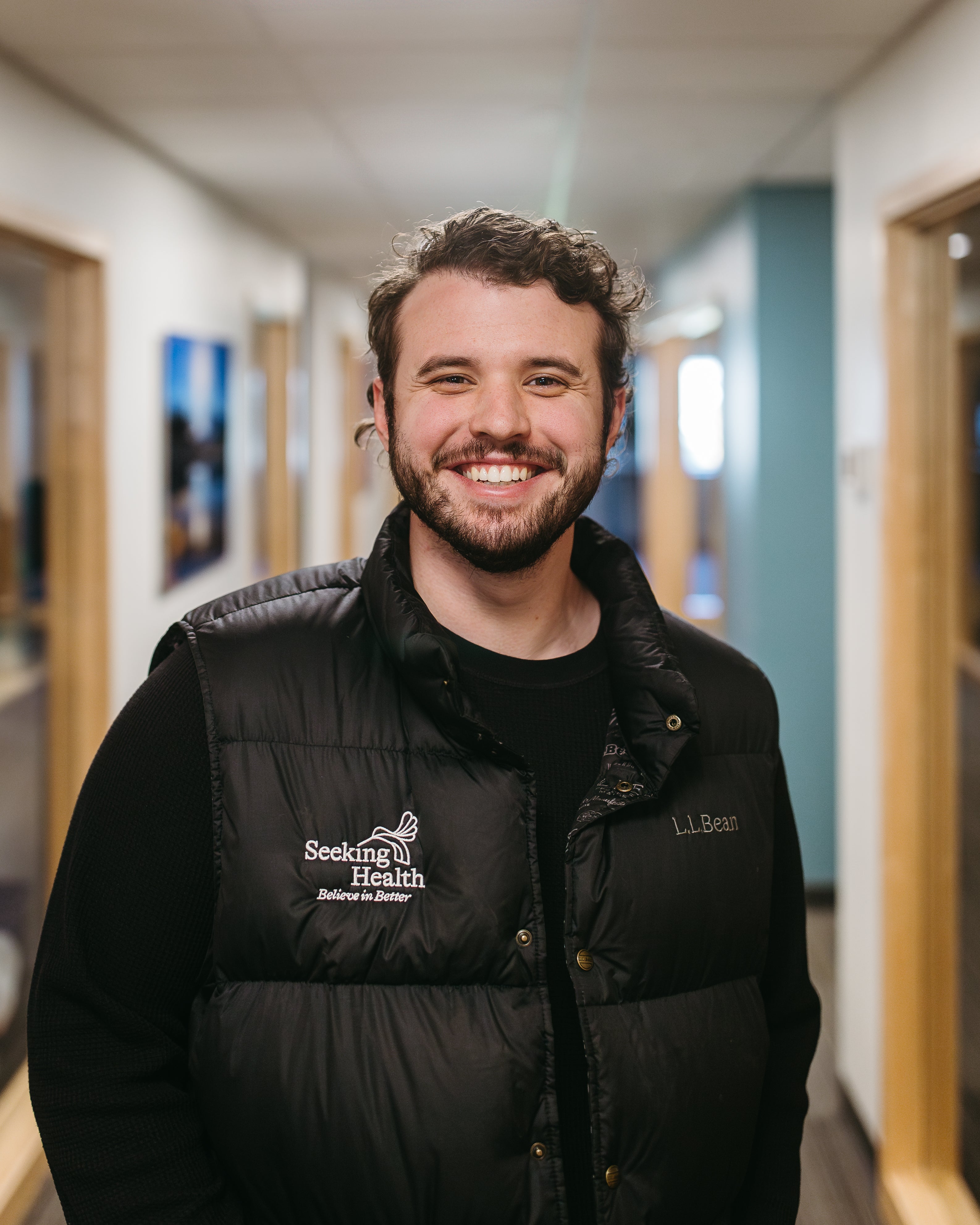 Man wearing a black vest with 'Seeking Health' logo in a hallway