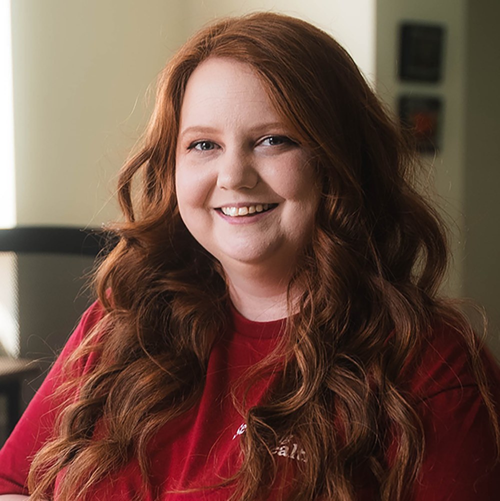 Person with long red hair wearing a red shirt indoors