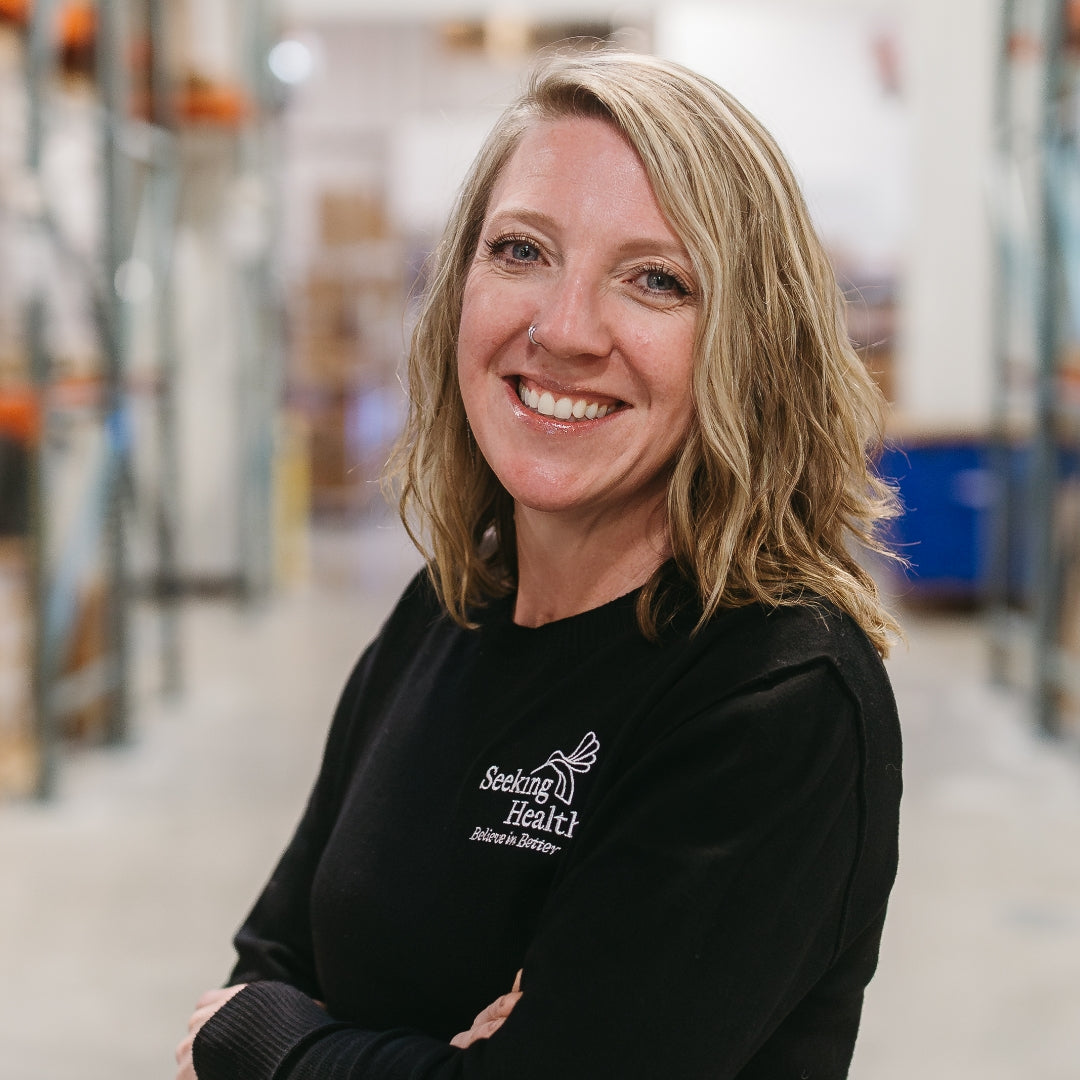 Woman wearing a black shirt with 'Seeking Health' logo in a warehouse setting