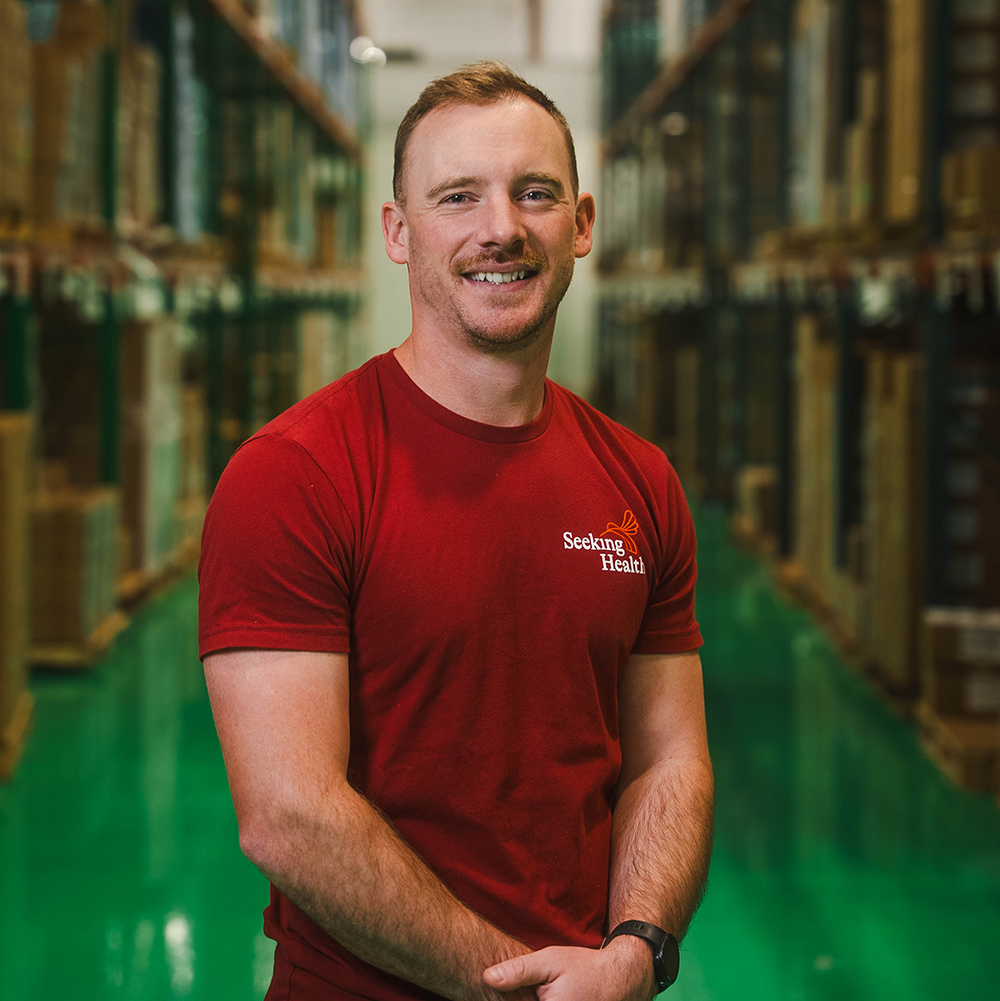 Man wearing a red 'Seeking Health' t-shirt in a warehouse setting