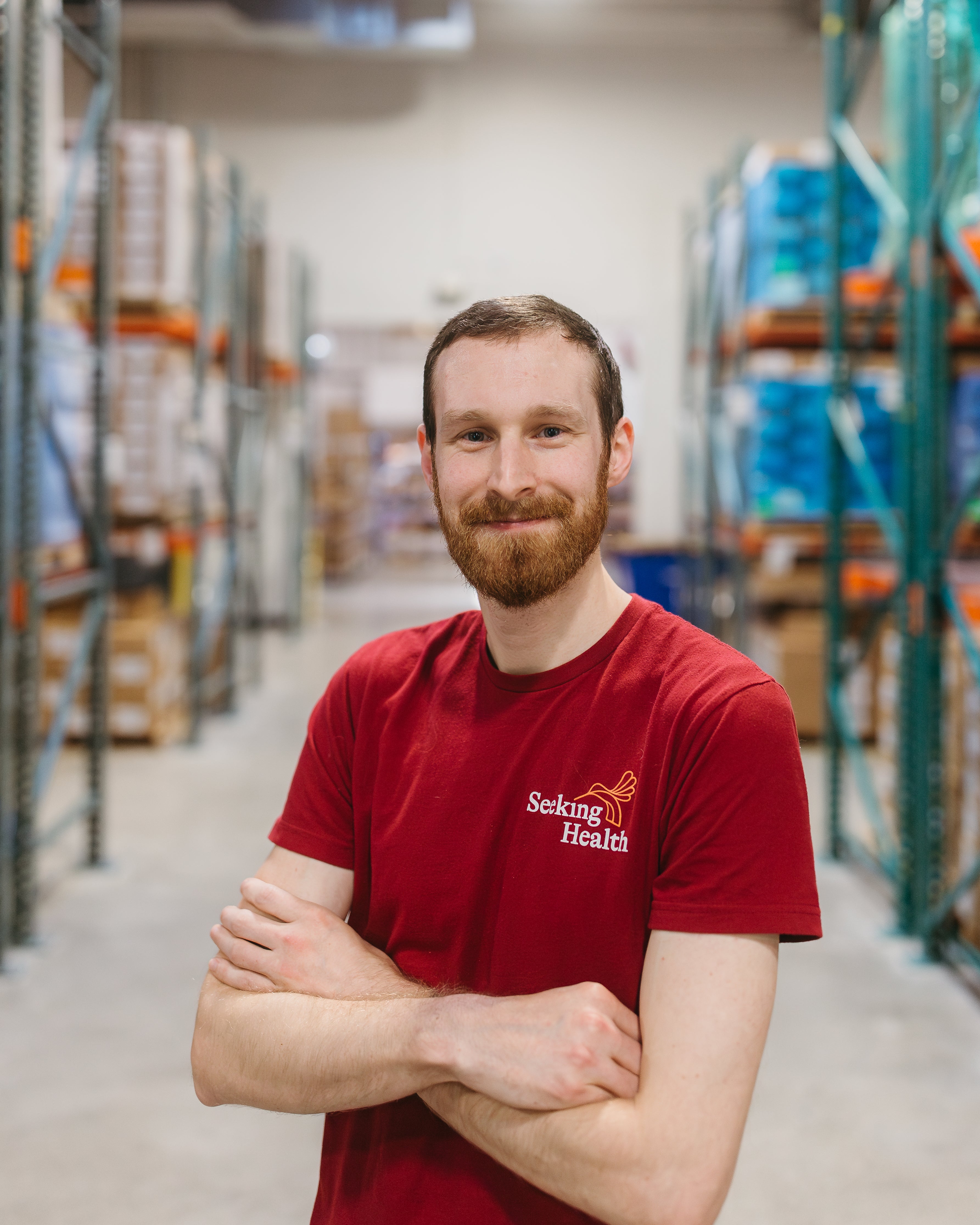 Man wearing a red 'Seeking Health' shirt in a warehouse setting