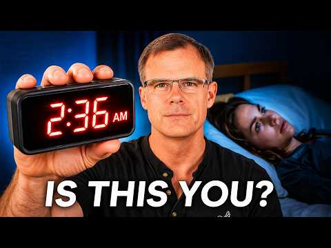 Man holding an alarm clock showing 2:36 AM with a woman lying in bed in the background.