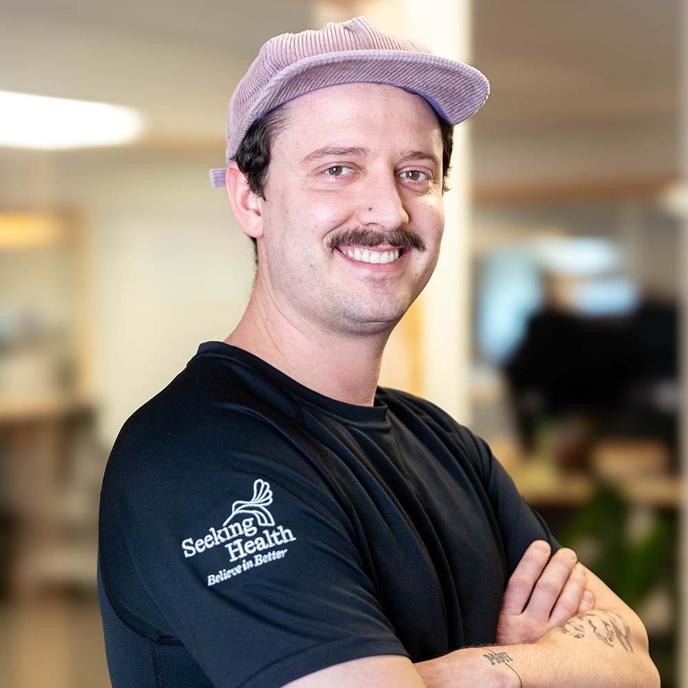 Man wearing a black 'Seeking Health' shirt with arms crossed indoors.