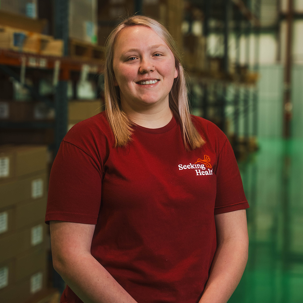 Person wearing a red 'Seeking Health' shirt in a warehouse setting
