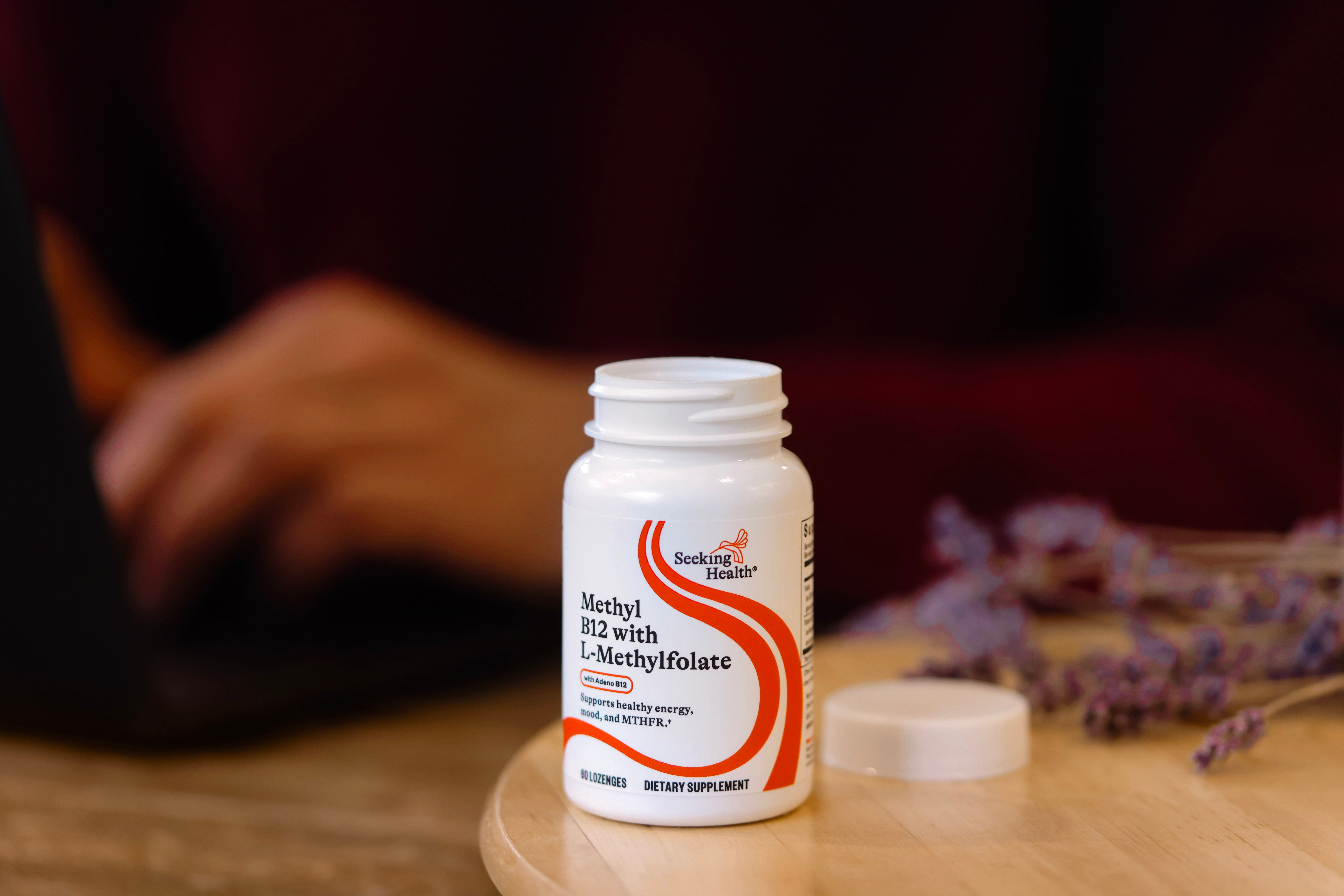 Supplement bottle labeled 'Sukin' on a wooden surface with blurred hands in the background