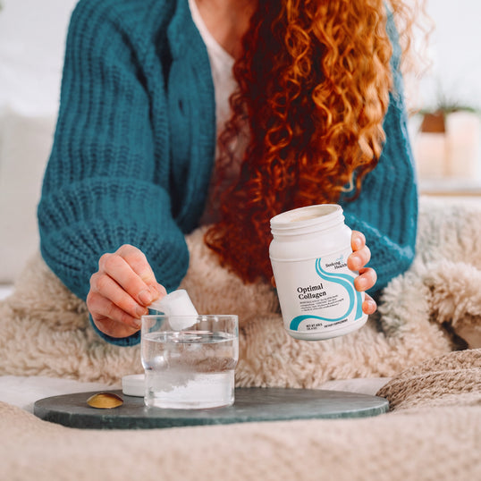 Person pouring Optima Collagen powder into a glass of water on a cozy couch.