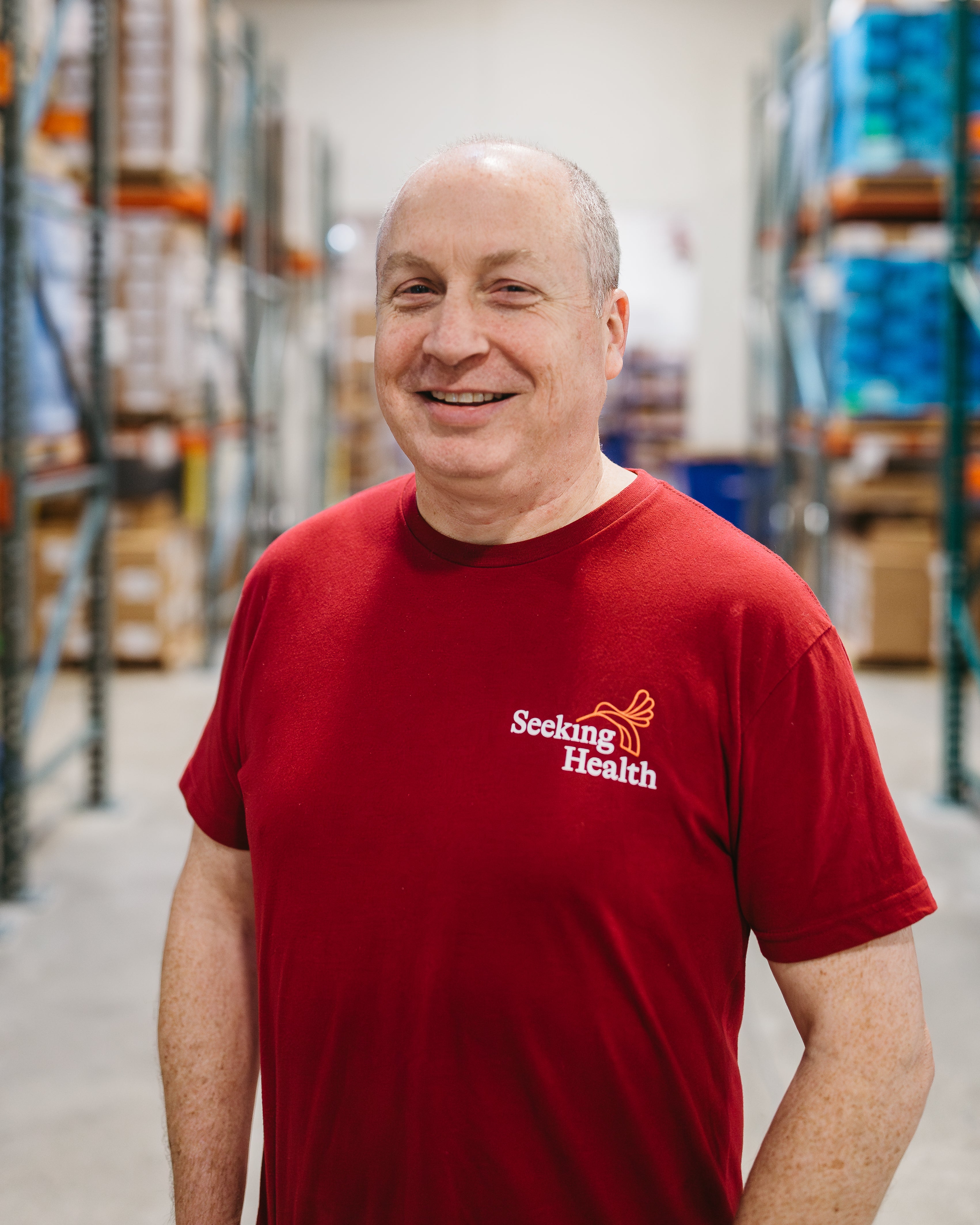 Man wearing a red 'Seeking Health' shirt in a warehouse setting