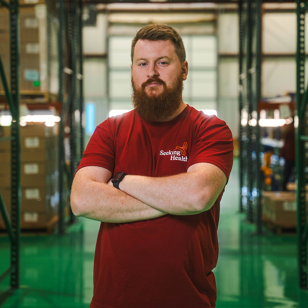Man wearing a red 'Seeking Health' shirt in a warehouse setting