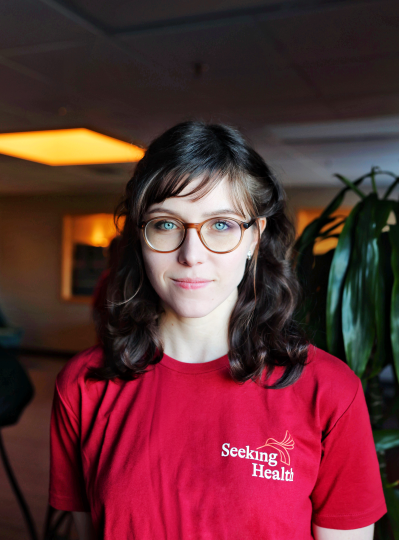Person wearing a red 'Seeking Health' t-shirt indoors with plants in the background