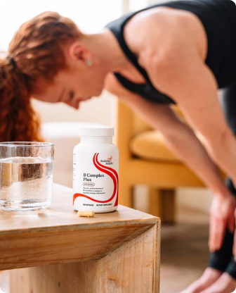 Person stretching with a container of B Complex Plus supplement on a table