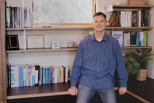 Dr. Ben Lynch seated in front of bookshelves
